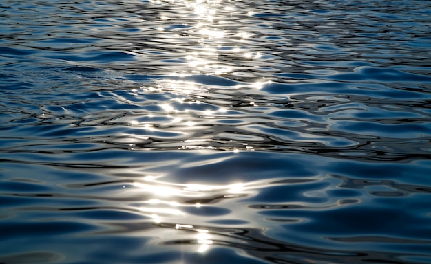Deep Blue water surface texture in sunset with sun rays reflection. 