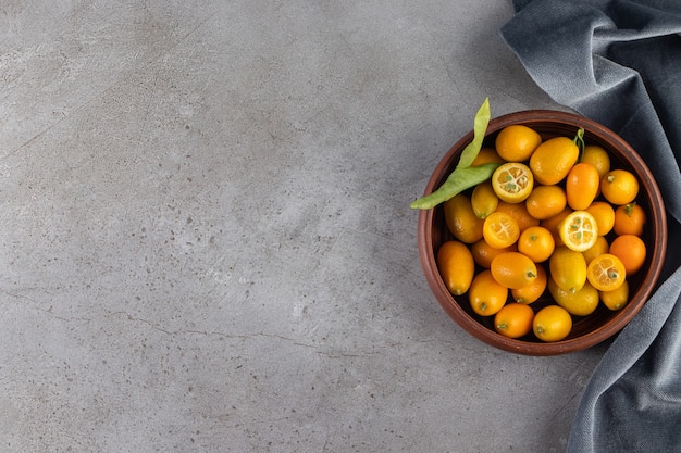 Deep bowl of fresh juicy kumquats on stone surface