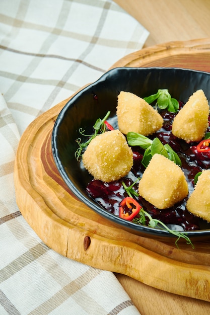 Deep fried crispy Camembert with cranberry sauce in a decorative pan on wooden board, Close up, selecive focus