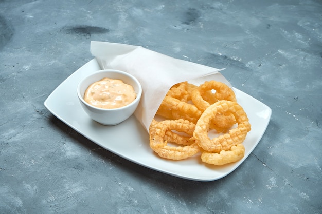 Deep-fried onion rings in a white plate on a gray background