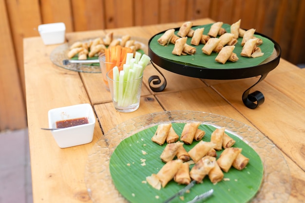 Involtini primavera fritti con verdure e vermicelli su piatto nero circolare con foglia di banana su un tavolo di legno all'aperto