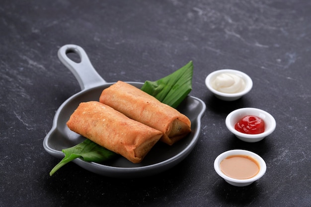 Lumpia 또는 Popia로 인기 있는 튀긴 스프링 롤. 회색 팬 플레이트, 검은색 대리석 테이블에 제공됩니다. 텍스트를 위한 공간 복사