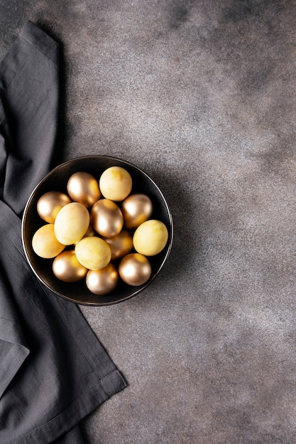 Фото Глубокая тарелка с золотыми пасхальными яйцами на темном бетоне