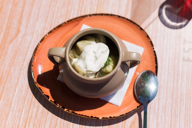 A deep plate with Siberian dumplings and sour cream on the table in an outdoor cafe