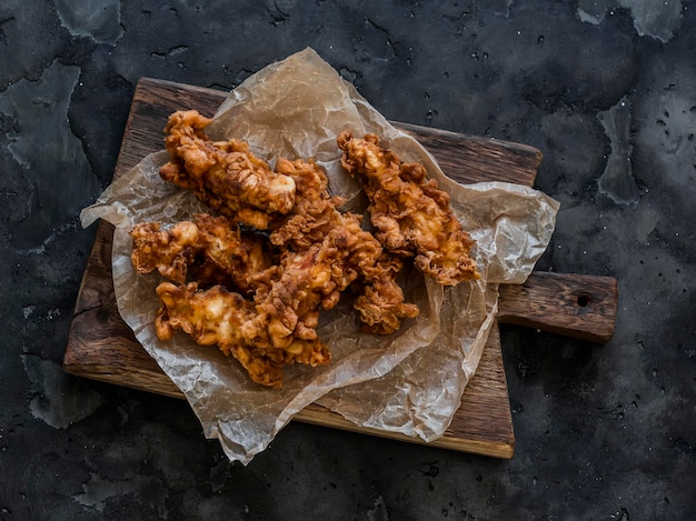 Foto pezzi di petto di pollo fritto in pasta deliziosi snack tapas su un taglialegna su uno sfondo scuro vista dall'alto