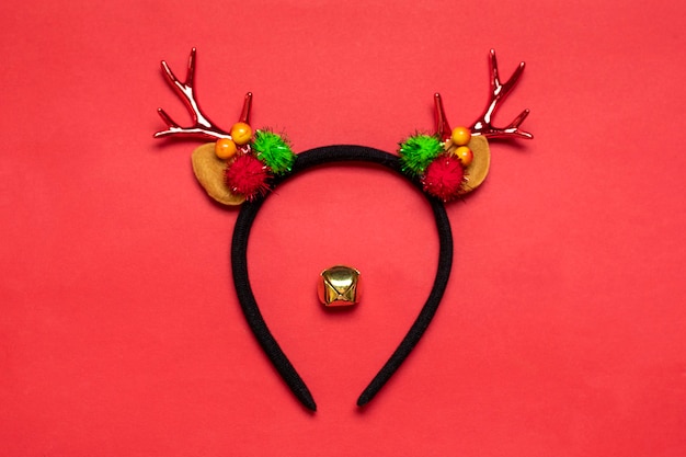 Deer muzzle made of rim with deer horns and ears, golden Christmas bell isolated on red background