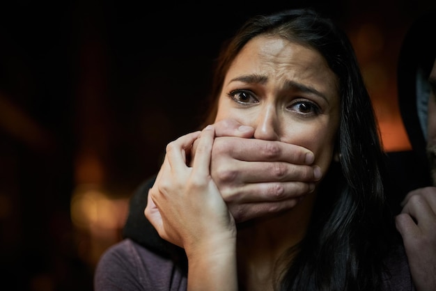 Defenceless and in danger Portrait of a frightened young woman with her assailants hand over her mouth