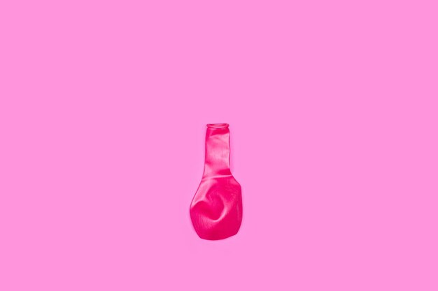 A deflated pink balloon on a pink background with copy space