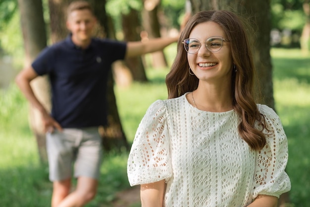 L'uomo sfocato si concentra sulla donna sorridente nel parco tra gli alberi la gente felice che si diverte il giorno d'estate coupl