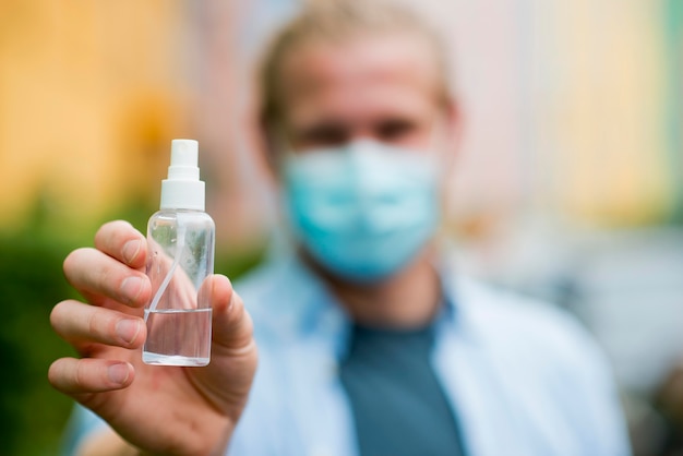 Uomo sfocato con disinfettante per le mani che tiene la maschera