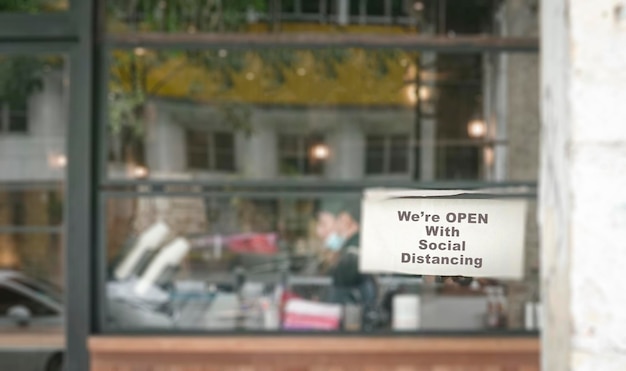 Defocused restaurant with notice on windows We're Open with Social Distancing