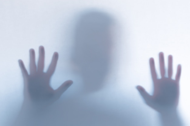 Defocused scary ghost silhouette behind a white glass