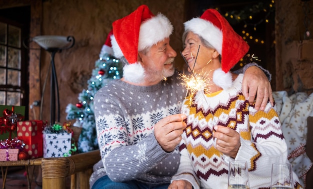 線香花火とクリスマスの時期に家で笑顔と抱擁サンタの帽子の焦点がぼけた年配のカップルクリスマス家族愛の概念線香花火に焦点を当てる