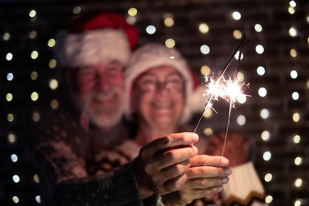 サンタ帽子をかぶったデフォーカスのシニア家族カップルがクリスマスと新年の夜を祝い、線香花火を発射する