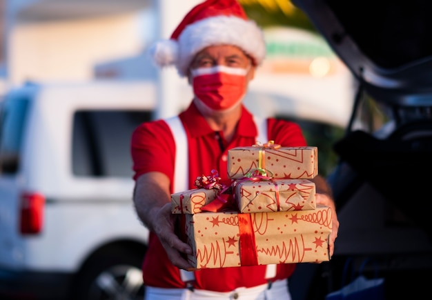 サンタの帽子と贈り物を保持しているサスペンダーでクリスマスの買い物をする焦点がぼけた年配の男性