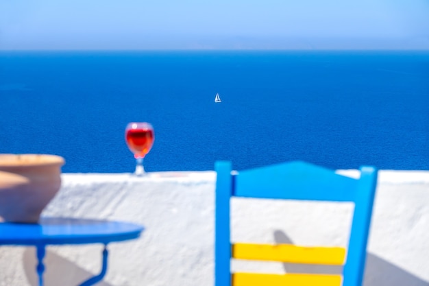 Foto defocused stoel, tafel en glas wijn en een wit zeiljacht ver in de zee