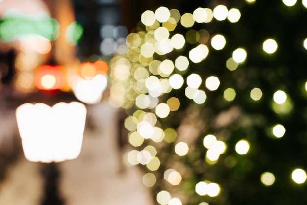 Defocusing Christmas lights, decorated with glowing Christmas tree at night outdoors. Blurred xmas abstract festive background