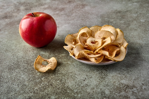 접시에 있는 탈수된 사과 칩과 나무 배경에 있는 사과 과일이 닫힙니다.