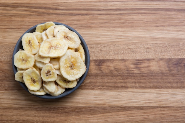 Foto chip disidratati e secchi della banana sul bordo di legno. vista dall'alto.