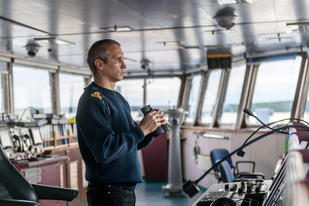 Dekofficier met verrekijker op navigatiebrug Zeeman aan boord van het schip Commerciële scheepvaart