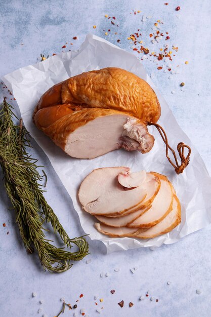 Photo deli meat smoked chicken breast sliced on white parchment surrounded by herbs and spices