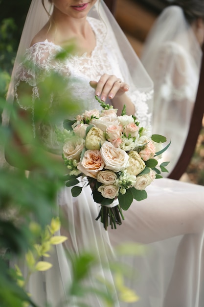 Delicaat bruidsboeket van witte, roze en poederachtige rozen in de handen van de bruid.