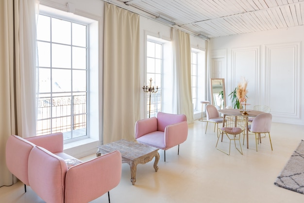 Delicaat en gezellig licht interieur van de woonkamer met modern stijlvol meubilair van pastelroze kleur en witte muren met stucwerk bij daglicht