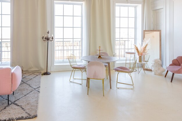 Delicaat en gezellig licht interieur van de woonkamer met modern stijlvol meubilair van pastelroze kleur en witte muren met stucwerk bij daglicht