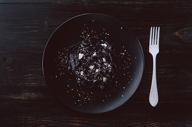 Delicacy black homemade pasta with feta cheese and Provencal herbs on a black plate