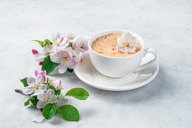 Delicate, beautiful flowers and a cup of cappuccino on a light gray wall. Side view.