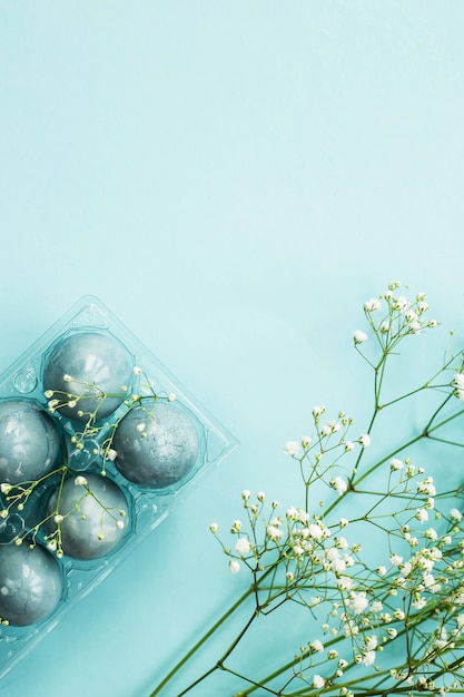 Delicate blue Easter eggs among the flowers of gypsophila on a blue background.