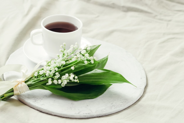 사진 실크 리본과 갓 양조 한 커피로 장식 된 계곡의 신선한 백합의 섬세한 꽃다발