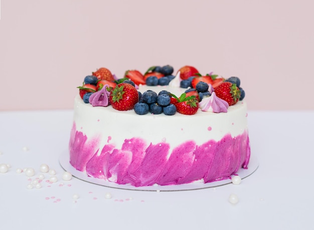 Delicate cake decorated with fresh berries strawberries and blueberries on a light plain background