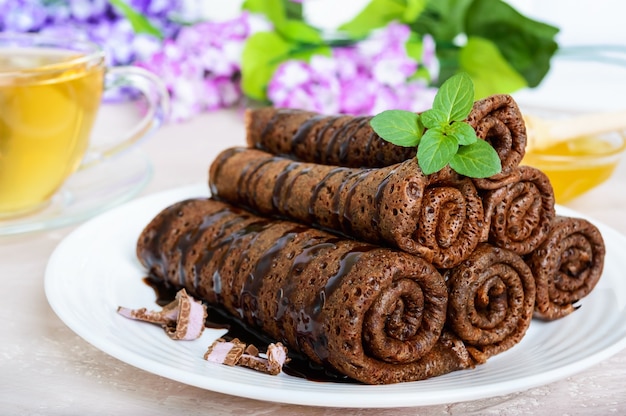 Delicate chocolade pannenkoeken gerold in een stapel en een kopje kruidenthee met honing