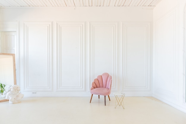 Photo delicate and cozy light interior of the living room with modern stylish furniture of pastel pink color and white walls with stucco moldings in daylight