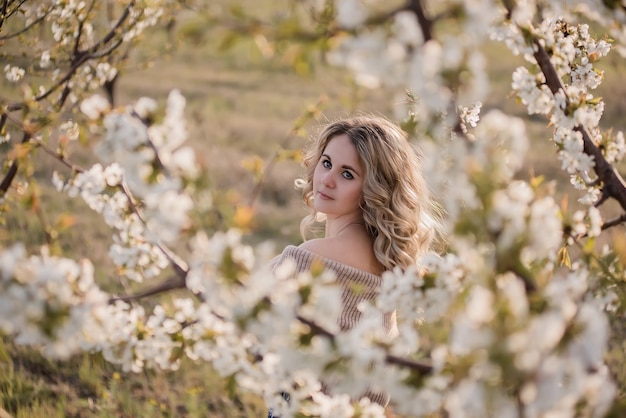 Delicate, dreamy girl with curly blond hair in blooming white gardens at sunset