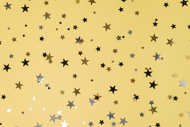 Delicate glitter star confetti on yellow table.