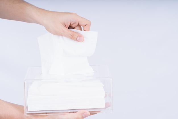 Delicate mannelijke handen die een wit tissuepapier uit een transparante doos van kristalweefsel trekken