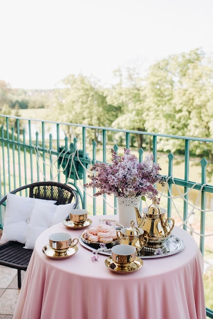 Delicate morning tea table setting with lilac flowers in Nesvizh castle, antique spoons and dishes on the table with a pink tablecloth.