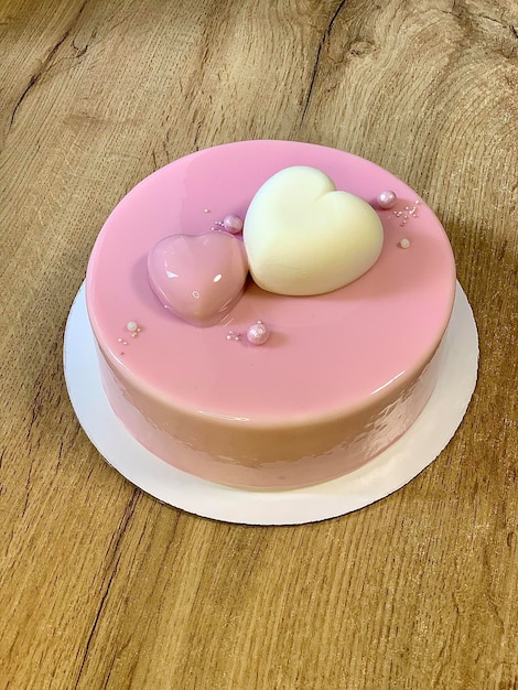 Delicate mousse cake with hearts covered with pink mirror glaze on a wooden tabletop, top view