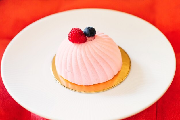 大きな白い皿に繊細なピンクのミニケーキ、柔らかい赤い椅子にデザートのプレート
