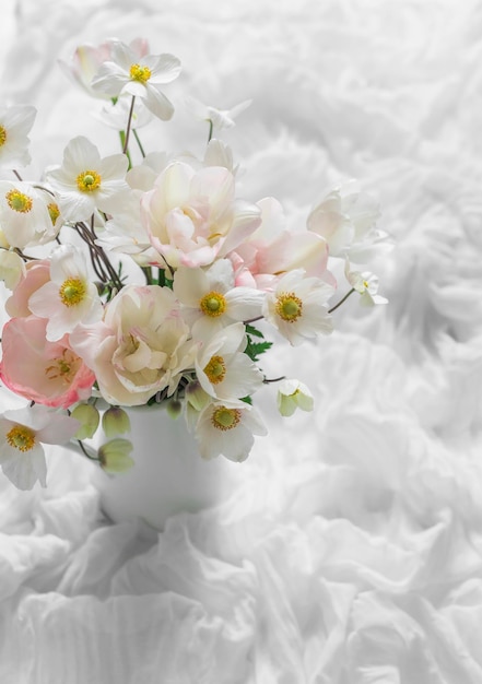 Delicate summer garden flowers in a jug on the table with a white airy tablecloth