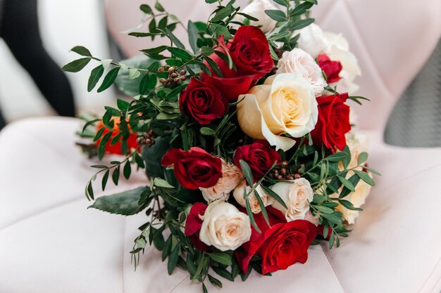 Foto delicato bouquet di nozze di rose beige e rosse su una poltrona di pelle bianca