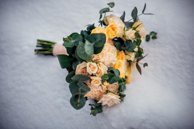 Delicate wedding bouquet of fresh flowers on fluffy snow, close-up. Beige roses on white frozen background. Winter wedding. Copy space.