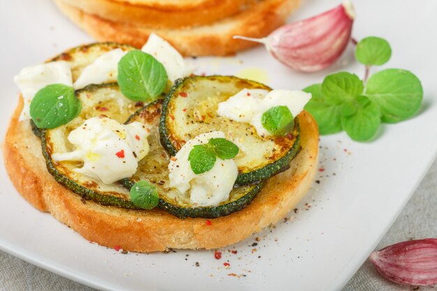 Delicatessebruschetta met gebakken of gebakken courgette, mozzarellakaas, knoflook, munt en kruiden. mediterraan broodje.