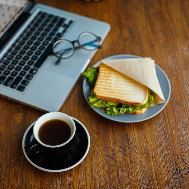 맛있는 아메리카노 커피, 식욕을 돋우는 샌드위치와 노트북이 있는 나무 테이블에 배열