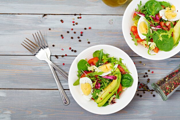 Вкусный и легкий салат из помидоров, яиц и микс листьев салата. здоровый завтрак. вид сверху