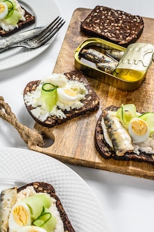 Deliziose tapas di antipasti, uova sode e sandwich di sardine in scatola. insalata con spinaci e pomodori secchi. sfondo bianco. vista dall'alto