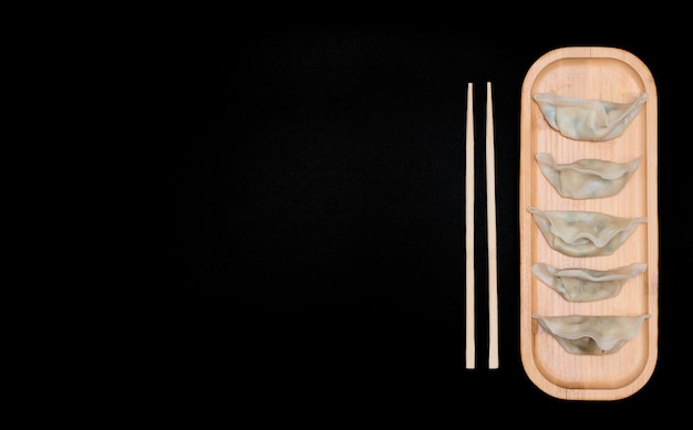 Delicious asian dumplings on wooden plate with chopsticks on black background Selective focus Asian food concept