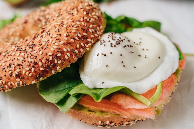 Delicious bagel with sesame and chia bread, inside it contains salmon, fried egg and basil